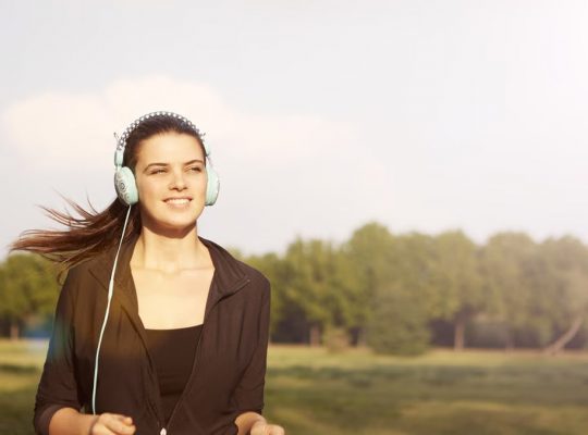 Smiling woman jogging in a park, listening to music with headphones, and enjoying the sunny day.