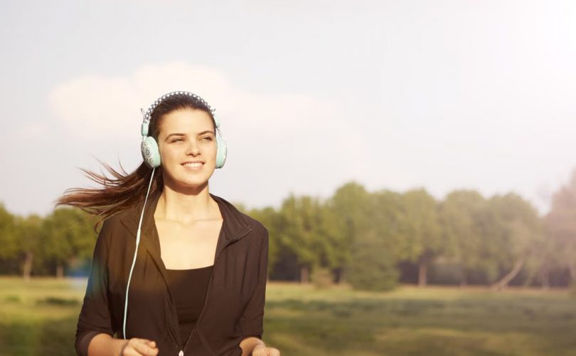 Smiling woman jogging in a park, listening to music with headphones, and enjoying the sunny day.