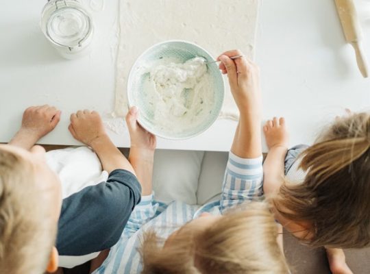 Three children mixing ingredients for homemade pastry in a bright kitchen setting.