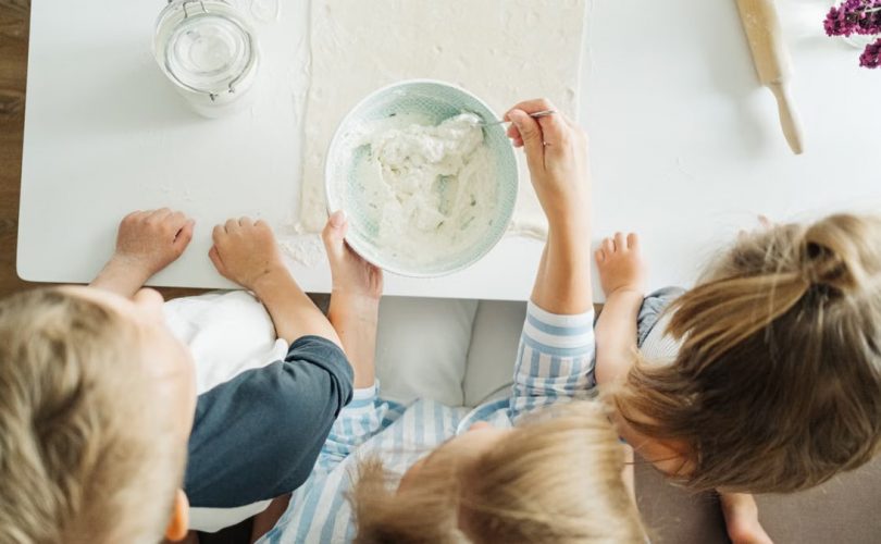 Three children mixing ingredients for homemade pastry in a bright kitchen setting.